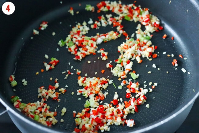 Sautéed garlic, ginger, green onions and red chilies in a pan.