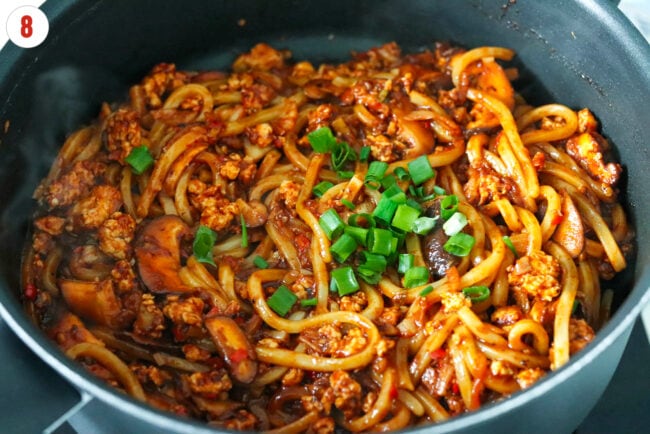 Added green onions to spicy kimchi chicken udon noodles in a pan.