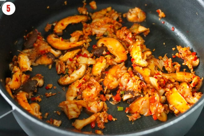 Sautéed mushrooms, kimchi, garlic, ginger, spring onion and red chilies in a skillet.