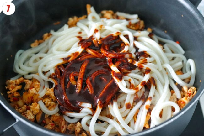 Spicy gochujang sauce and cooked udon noodles in a pan with stir-fried kimchi and chicken.
