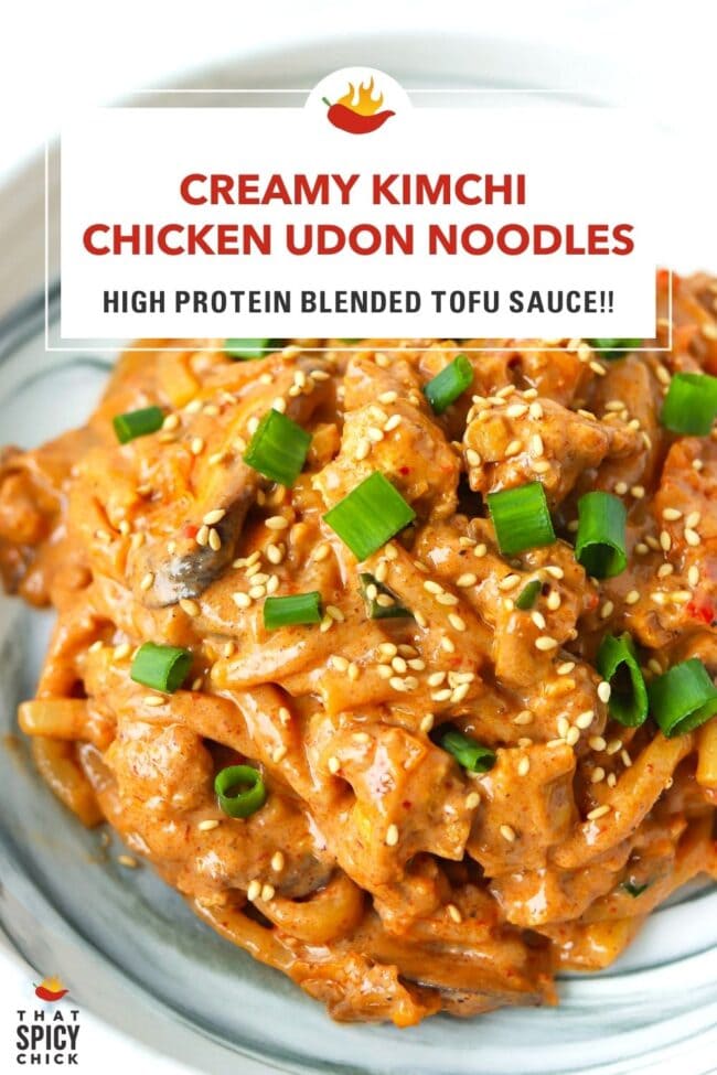 Front view closeup of creamy kimchi noodles with chicken garnished with green onions and sesame seeds on a plate. Text overlay "Creamy Kimchi Chicken Udon Noodles", "High Protein Blended Tofu Sauce!!" and "That Spicy Chick".