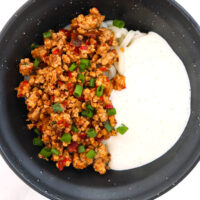 Mapo seasoned pork garnished with green onions, udon noodles, and silken tofu sauce in a black bowl.