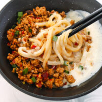 Chopsticks mixing silken tofu sauce with mapo pork and udon noodles.