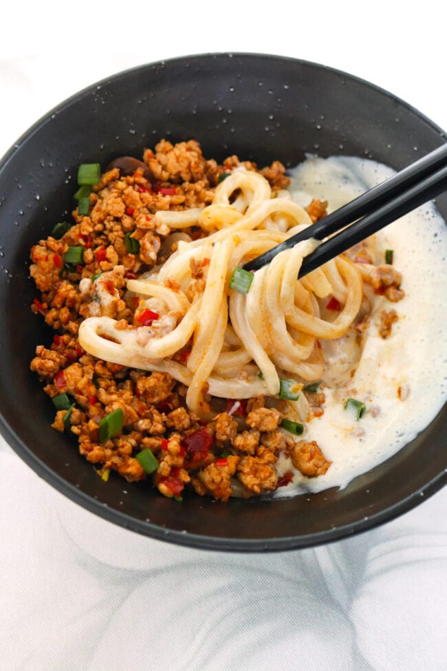 Chopsticks mixing silken tofu sauce with mapo pork and udon noodles.
