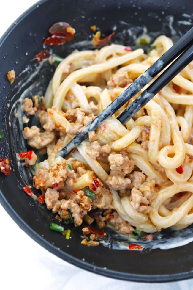 Closeup of creamy mapo tofu pork udon noodles in a black bowl with chopsticks.