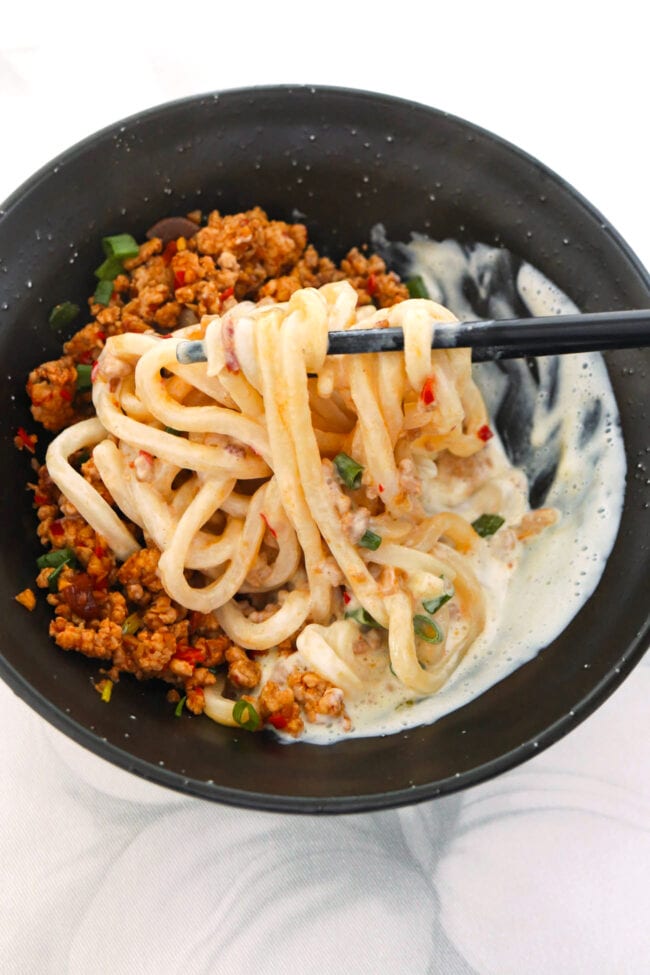 Chopsticks pulling up noodles from bowl with creamy mapo tofu udon.