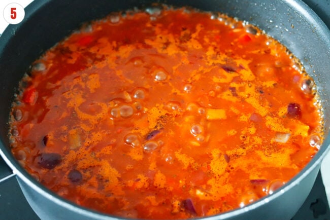Tomato broth boiling with vegetable in pan.