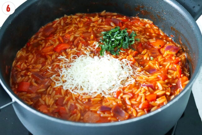 Grated parmesan and sliced basil added to skillet with Cajun sausage orzo.