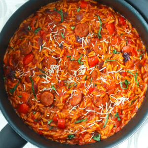 Cajun orzo with peppers and sausage in a black skillet.