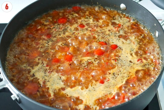 Broth base, cherry tomatoes and seasonings boiling in a pan.