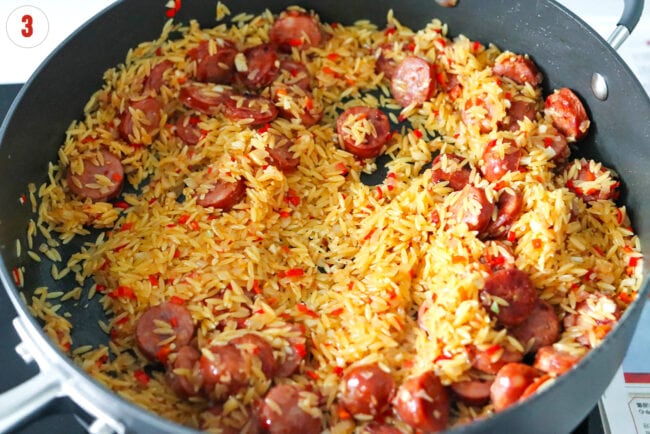 Toasting orzo in pan with sautรฉed garlic, onion, red chilies and spicy sausage.