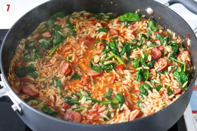 Wilted spinach in a pan with spicy sausage orzo.