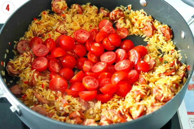 Cherry tomatoes in pan with sautรฉed sausage, orzo, onion, garlic and chilies.