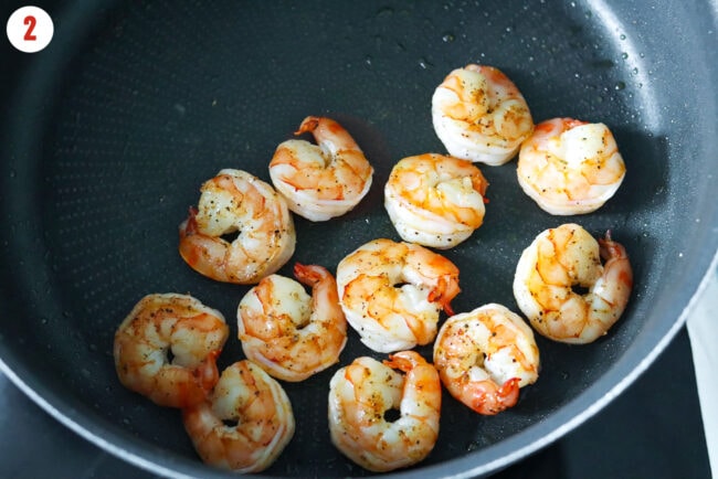 Cooked salt and pepper seasoned jumbo shrimp in a skillet.