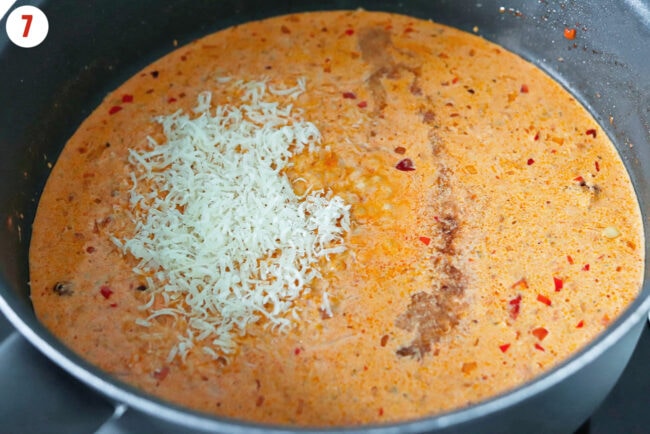 Grated Parmigiano Reggiano cheese and sherry vinegar in pan with creamy Calabrian chili pasta sauce.