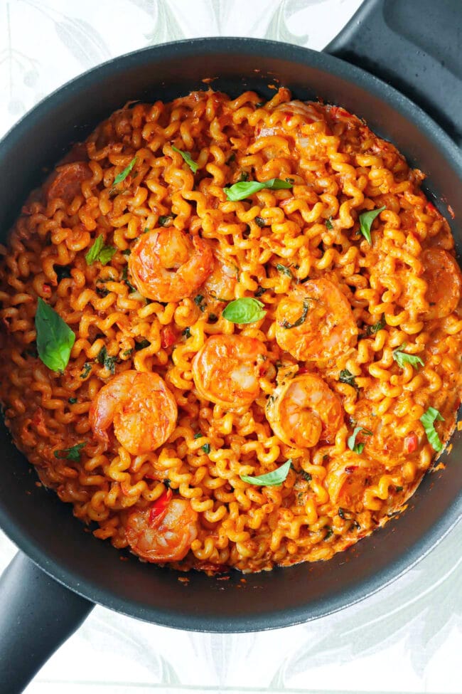 Top view of nonstick pan with creamy Calabrian chili pasta and shrimp garnished with fresh basil.