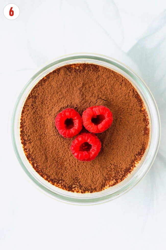 Single serving cottage cheese tiramisu dusted with cocoa powder and topped with raspberries.
