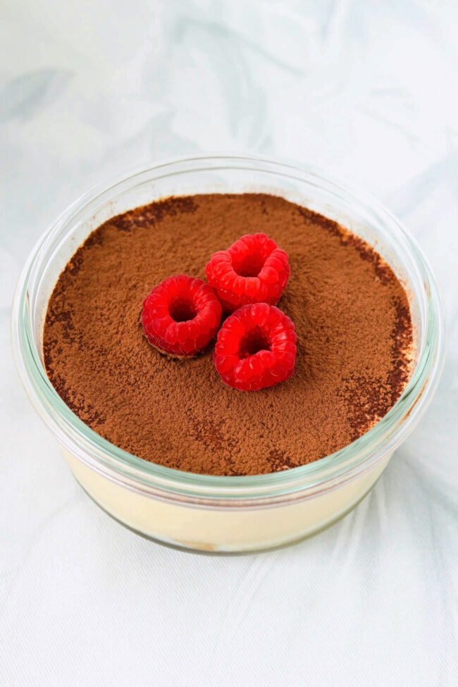 Cottage cheese tiramisu in a small round dish topped with cocoa powder and raspberries.