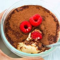 Hand holding small round dish with cottage cheese tiramisu and a spoon.