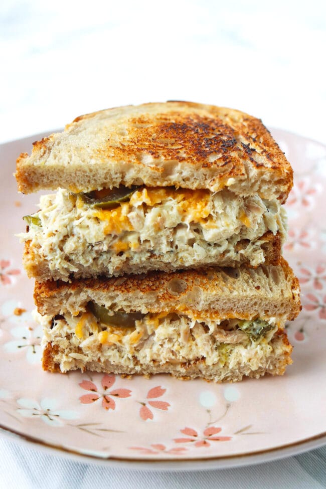 High protein tuna salad sourdough sandwich with melted cheddar cheese and pickled jalapeños stacked on a pink plate.