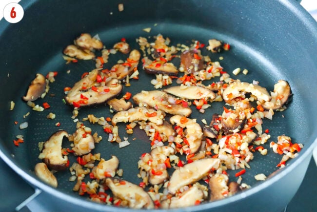 Sautéed shallots, garlic and chilies, and sliced shiitake mushrooms in a pan.