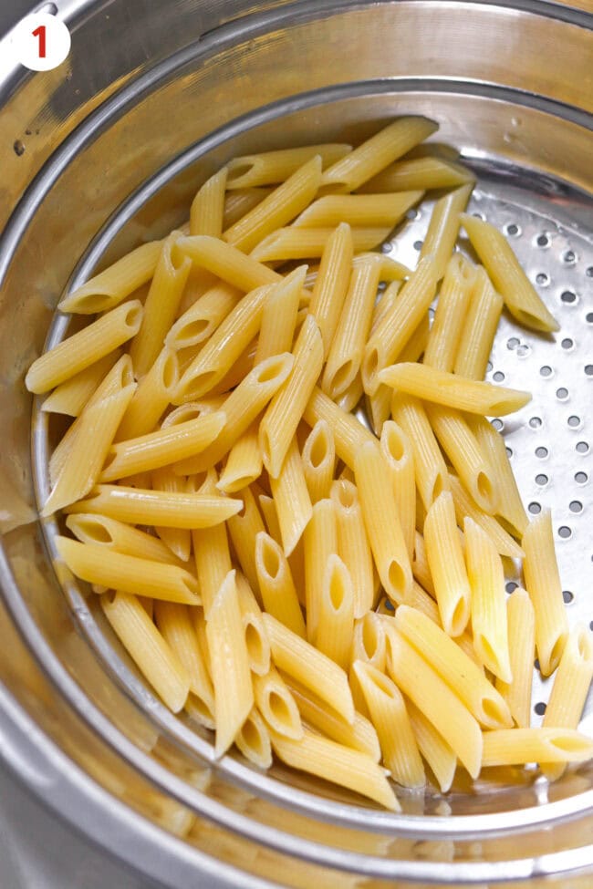 Cooked and drained penne pasta in a colander.