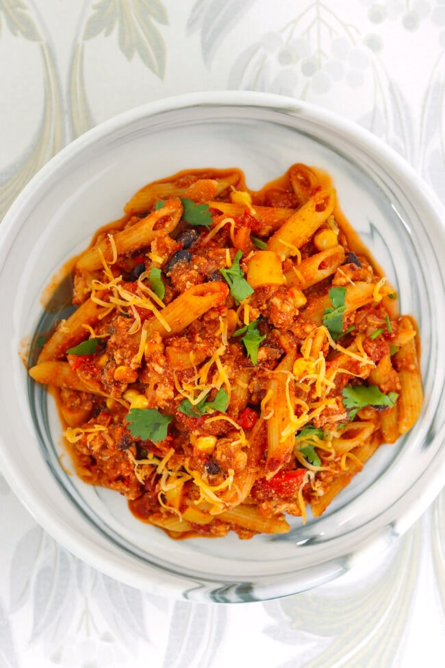 Plate with chicken taco pasta topped with shredded cheddar and fresh cilantro.