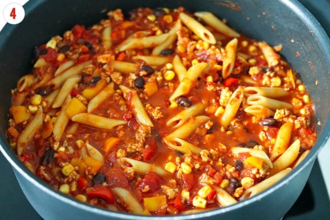 Spicy ground chicken taco pasta with tomatoes, corn and black beans in a pan on the stove.