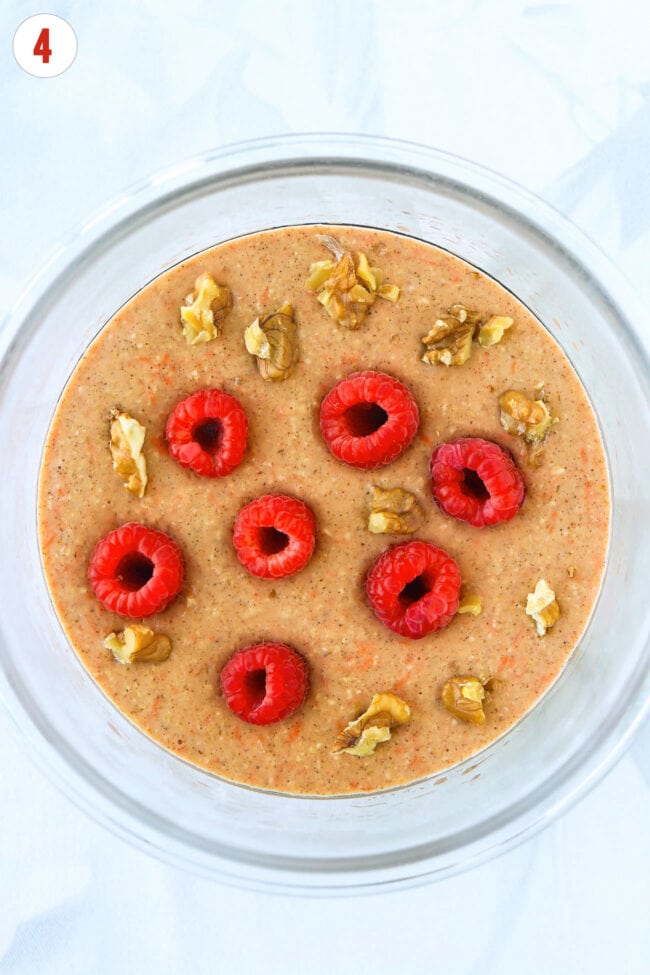 Carrot cake protein pancake batter in a round glass meal prep container topped with chopped walnuts and raspberries.