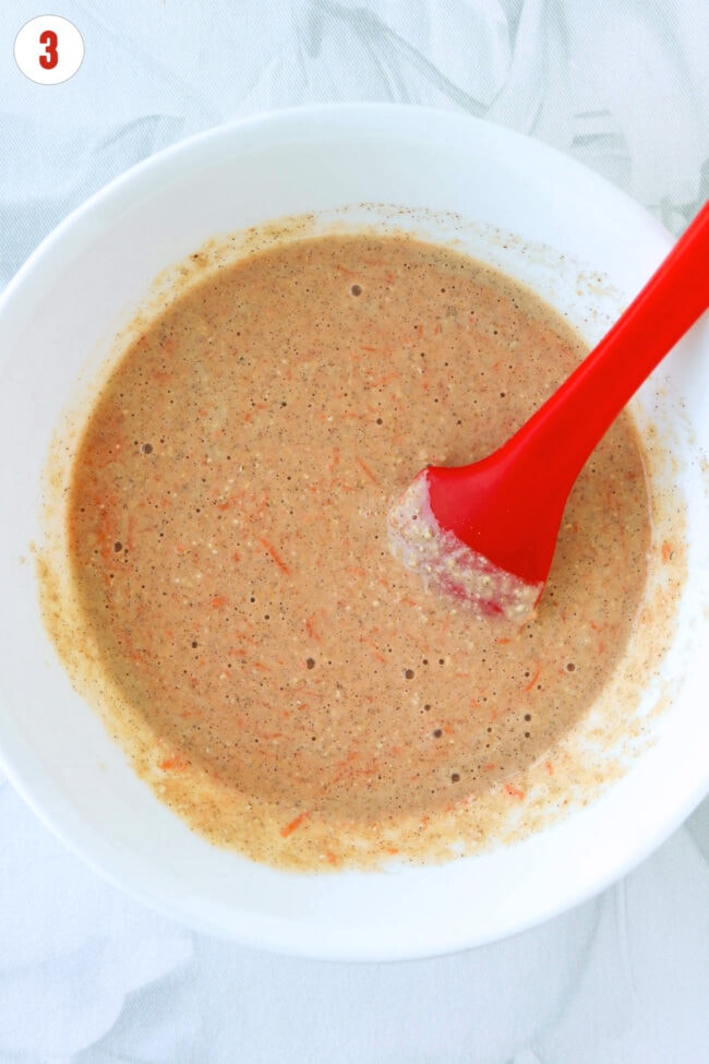 Protein pancake batter with grated carrots in a white bowl with a red silicone spatula.
