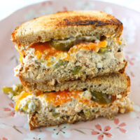 Healthy salmon salad toasted sourdough bread sandwich with cheddar cheese and pickled jalapeños stacked on a plate.