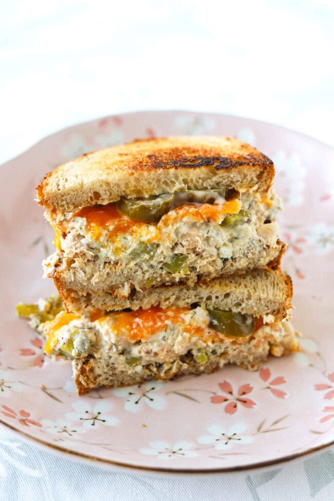 High protein salmon salad sourdough sandwich with melted cheddar cheese and pickled jalapeños stacked on a pink plate.