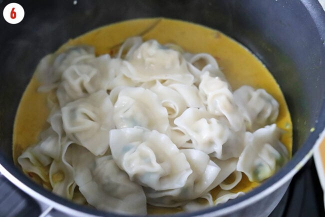 Cooked dumplings and noodles in a pot with curry sauce.