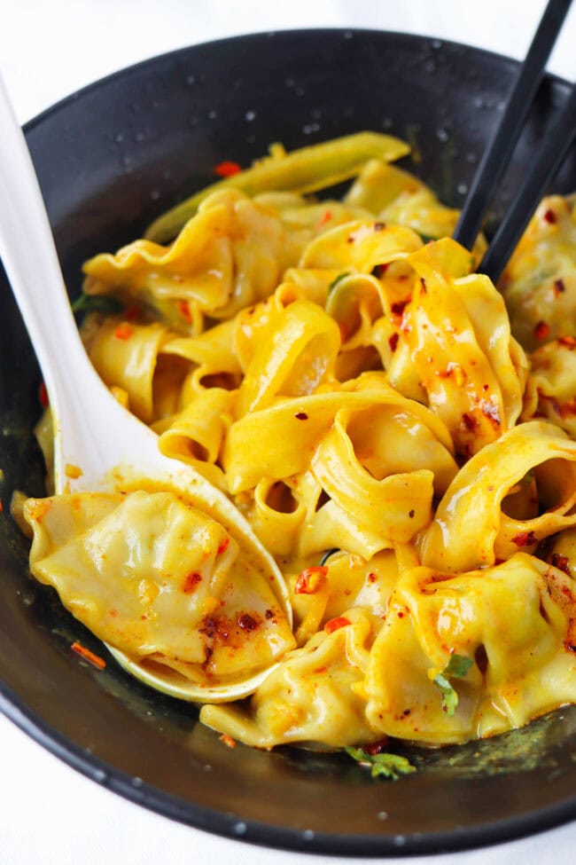 Closeup front view of black bowl with curry sauce dumplings and noodles topped with chili crisp.