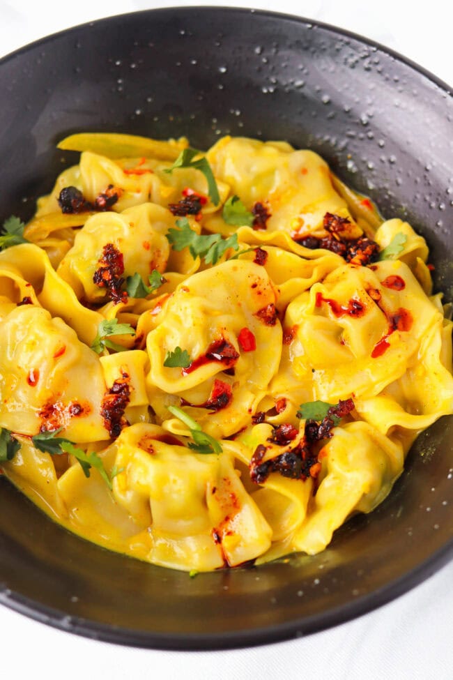 Front view of black bowl with curry sauce dumplings and noodles topped with chili crisp and cilantro.