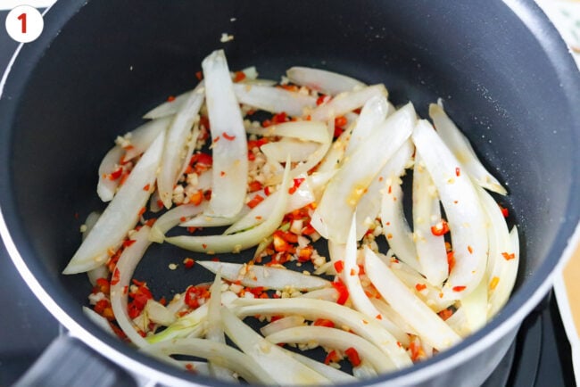Sautéed thick sliced yellow onion, garlic and red chilies in a pot.