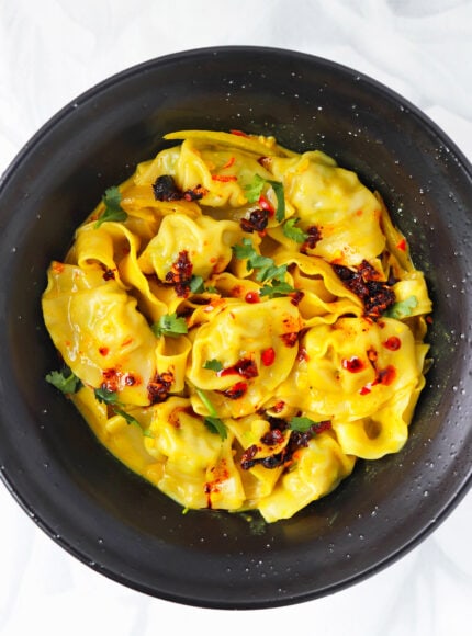 Curry dumplings with noodles topped with chili crisp and chopped cilantro in a black bowl.