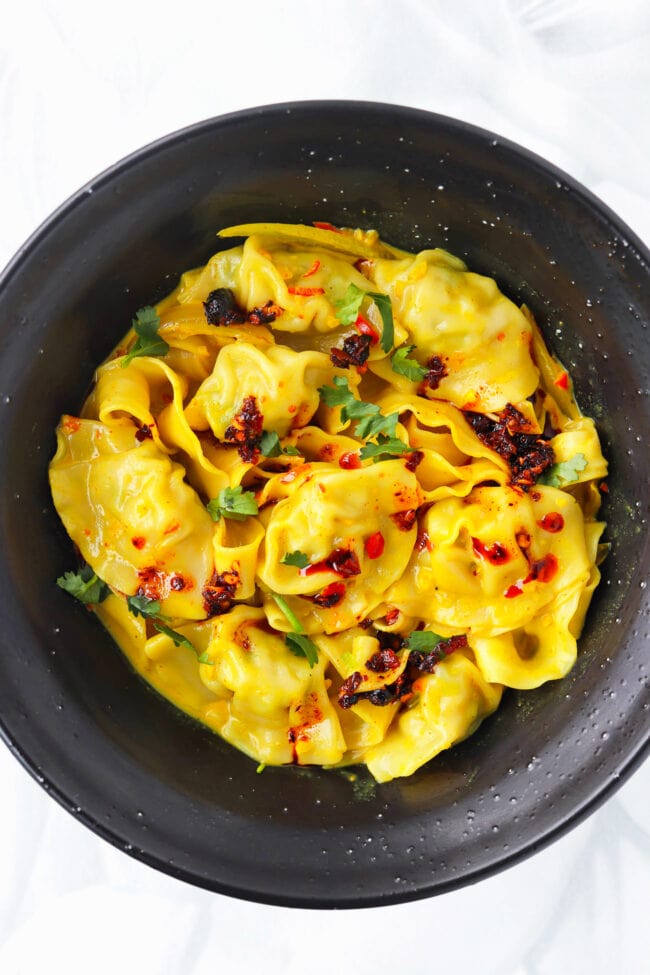 Closeup of curry dumplings with noodles topped with chili crisp and chopped cilantro in a black bowl.