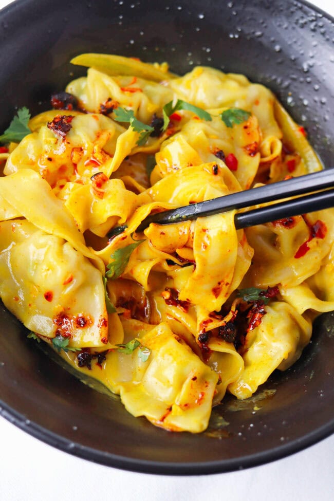Chopsticks pulling up noodles from bowl with curry sauce dumplings and noodles topped with chili crisp and cilantro.