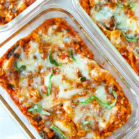 Closeup of vodka sauce lasagna topped with sliced basil in oven-safe dishes.
