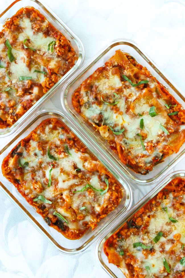 Meal prep containers with spicy vodka sauce lasagna topped with melted cheese and sliced basil.