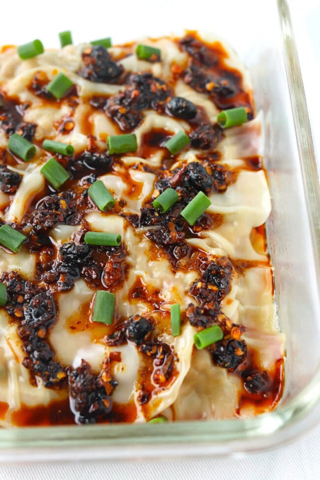 Closeup front view of dish with dumpling lasagna topped with chili crisp and spring onion.