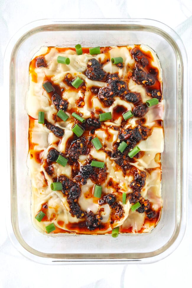 Closeup top view of dish with dumpling lasagna topped with chili crisp and spring onion.