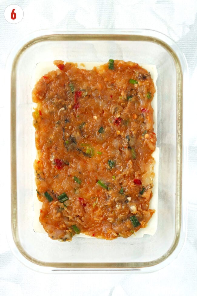 Chicken and shrimp filling layered on top of wonton wrappers in a glass baking dish.