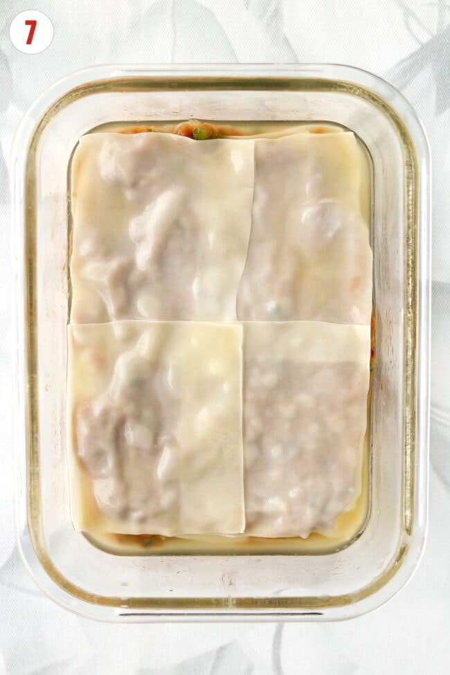 Assembled dumpling lasagna with top layer of wonton wrappers and water in a glass heatproof dish.