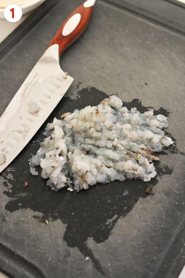Chopped shrimp paste and knife on a black chopping board.