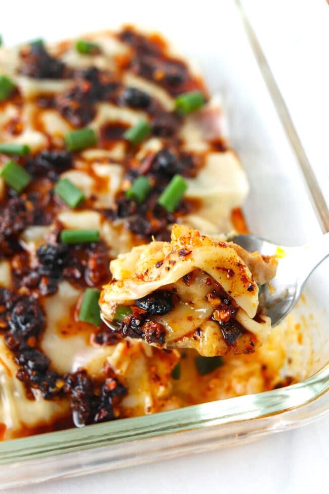 Closeup of spoon holding up a bite of dumpling lasagna topped with chili crisp above dish.