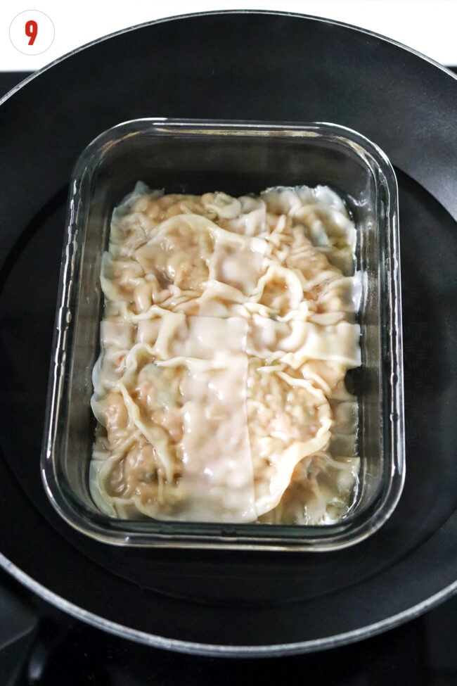 Steamed dumpling lasagna in a glass dish in wok filled with water.