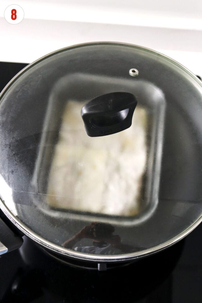 Dumpling lasagna steaming in a covered wok filled with water.
