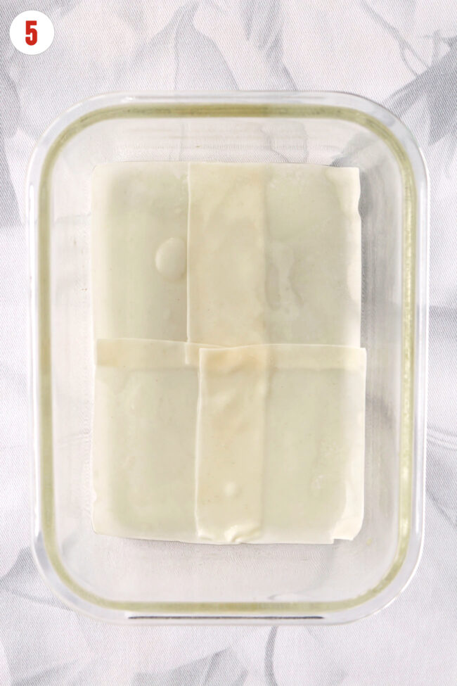 Four lightly wet wonton wrappers layered in a heatproof glass dish greased with sesame oil.